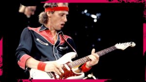 Mark Knopfler con cinta en el pelo tocando la guitarra